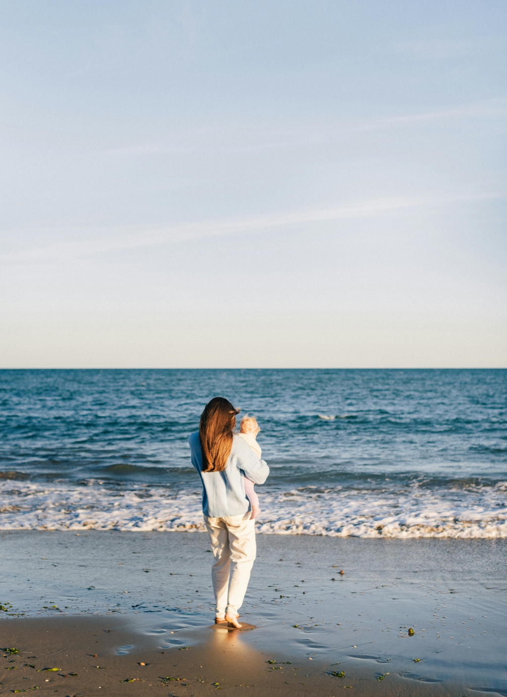 A mother on a beach with her baby. Relates to Niss trying to escape the harsh layer poultry business struggles and reconnect with nature.